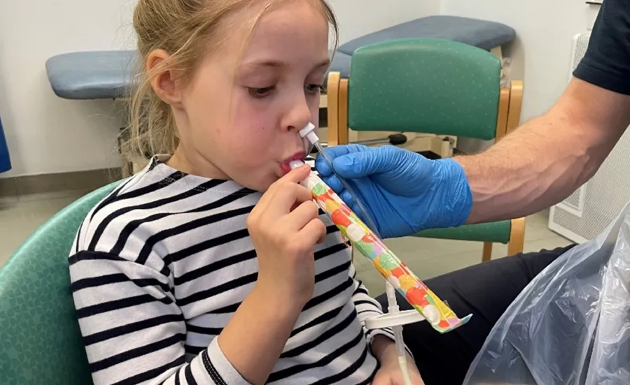 Young girl with a tube up her left nostril, blowing a party blower